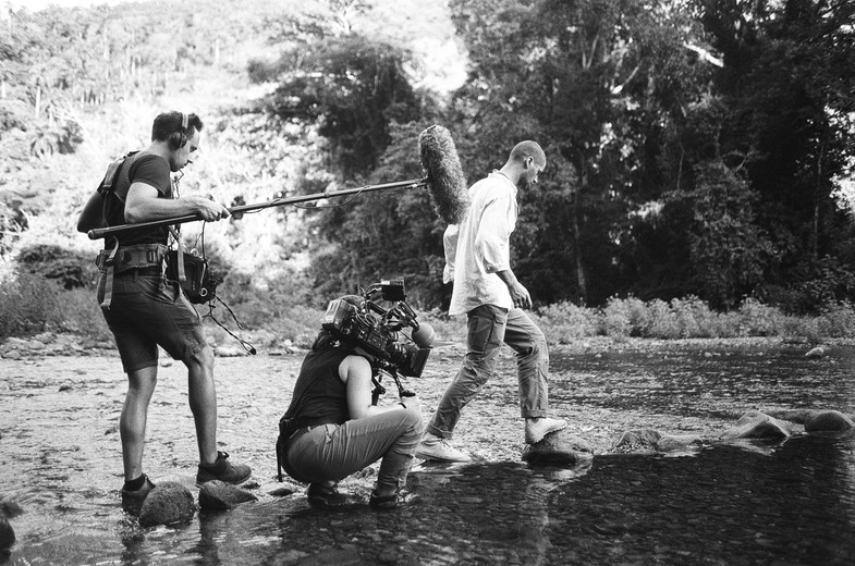 Équipe de tournage traversant une rivière au bord d'une forêt tropicale
